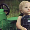 Farm Kids | A photograph of a small child sitting in a field with a green toy tractor. | Harrowsmith Magazine